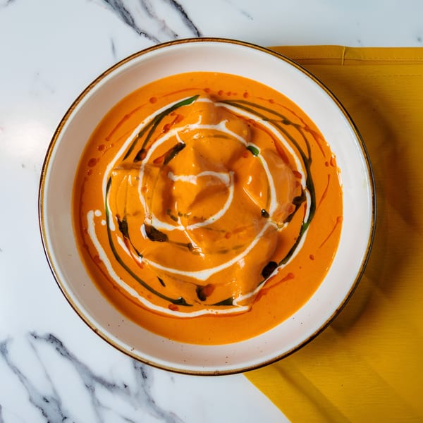 Overhead view of a bowl of orange curry with white and green swirls, on a marble table.