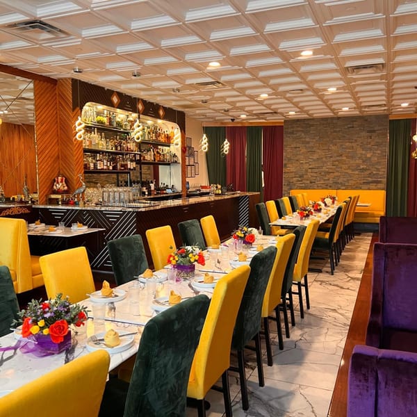A vibrant restaurant interior with yellow and dark green chairs, set tables, a bar, and stone accent walls.