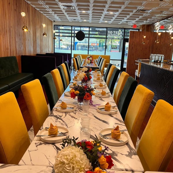 Long dining tables with yellow and black chairs, set with plates, silverware, and floral centerpieces.