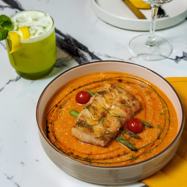 Pan-seared fish with cherry tomatoes and green beans in a red sauce, alongside a green cocktail.
