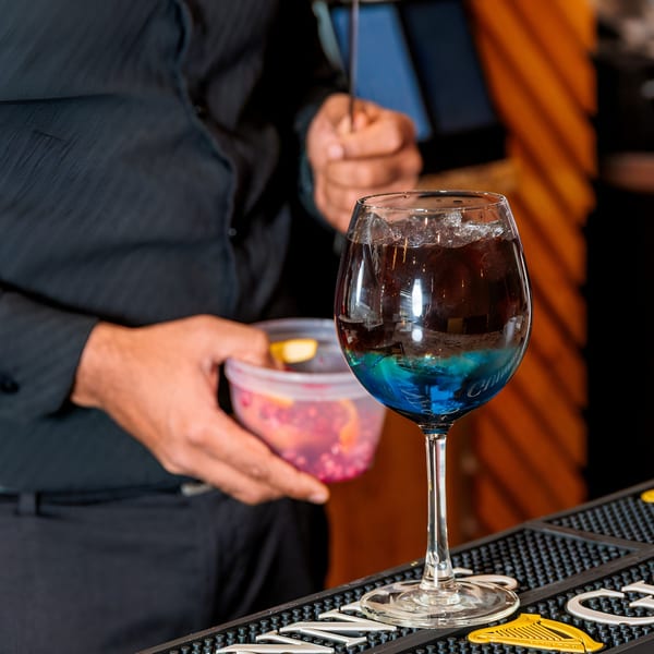 Bartender preparing a blue and brown layered cocktail in a large wine glass at Ssaanjh Indian.