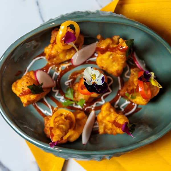 Golden fried pakoras drizzled with sauces and garnished with edible flowers and radish slices.
