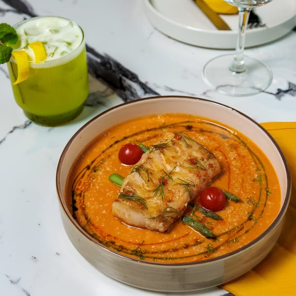 Pan-seared fish in a creamy orange sauce with cherry tomatoes, green beans, and a green cocktail.