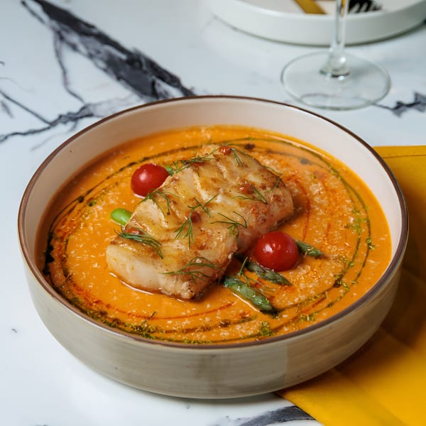 Pan-seared fish fillet in a vibrant orange sauce, garnished with cherry tomatoes and asparagus.