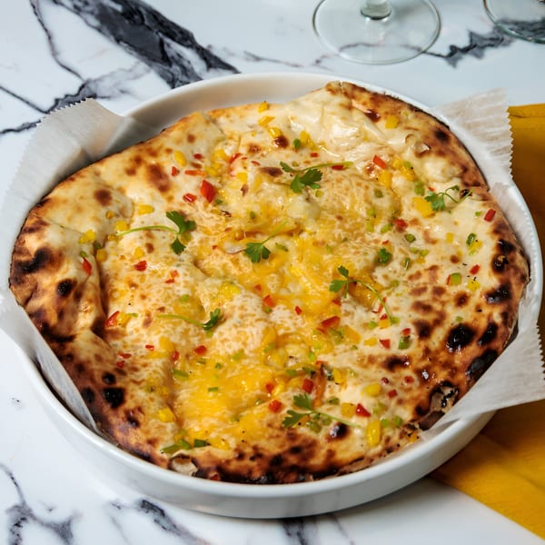 Cheesy naan bread topped with colorful diced bell peppers and fresh cilantro in a white bowl.